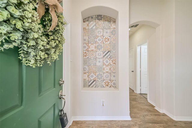 foyer with baseboards, visible vents, arched walkways, and light wood-type flooring