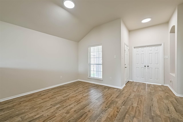 empty room with vaulted ceiling, wood finished floors, baseboards, and arched walkways