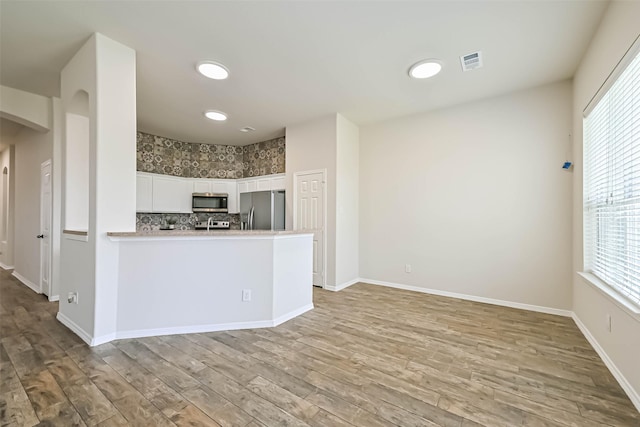 kitchen with light wood finished floors, a peninsula, arched walkways, stainless steel appliances, and light countertops