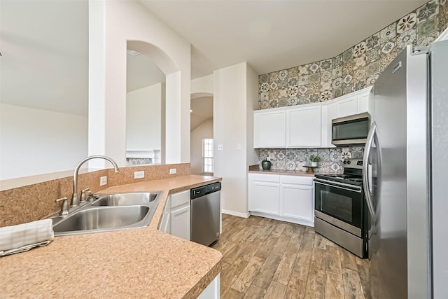 kitchen featuring a sink, stainless steel appliances, arched walkways, light wood-style floors, and white cabinets