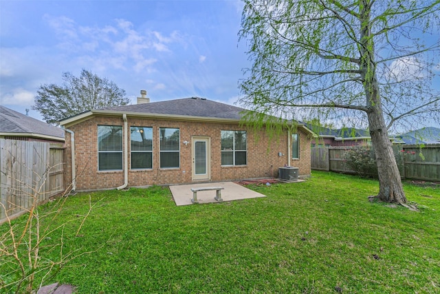 rear view of house with a lawn, a fenced backyard, brick siding, a chimney, and a patio area