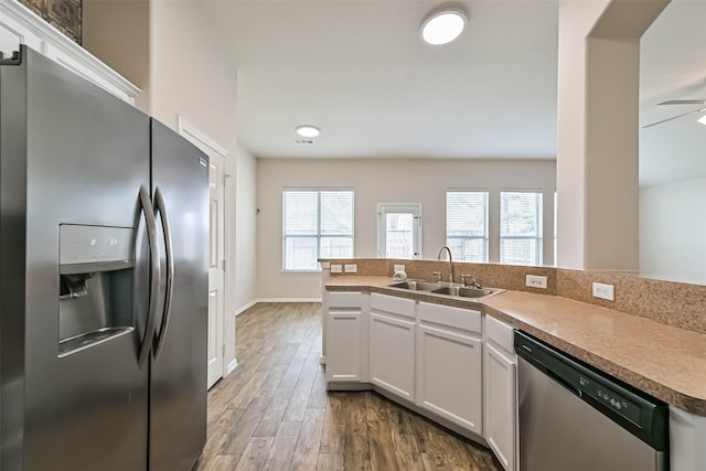 kitchen with a sink, wood finished floors, stainless steel appliances, white cabinets, and baseboards