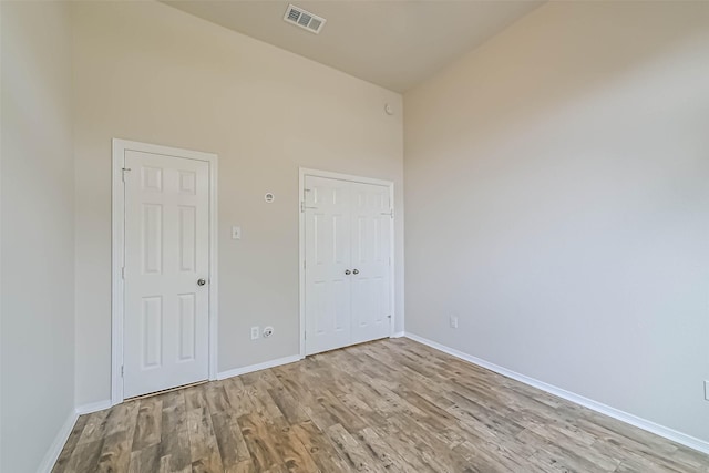 unfurnished bedroom featuring wood finished floors, visible vents, baseboards, a high ceiling, and a closet