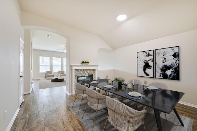 dining area with visible vents, lofted ceiling, a fireplace, wood finished floors, and arched walkways