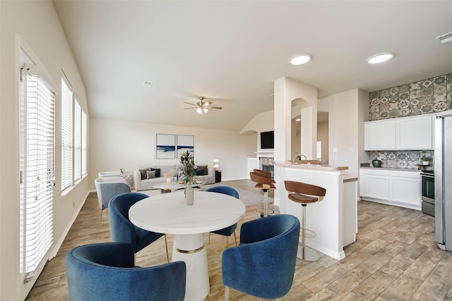 dining area with visible vents, light wood-type flooring, lofted ceiling, a fireplace, and a ceiling fan