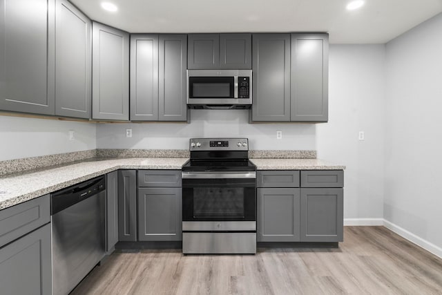 kitchen with gray cabinets, light stone counters, appliances with stainless steel finishes, light wood finished floors, and baseboards