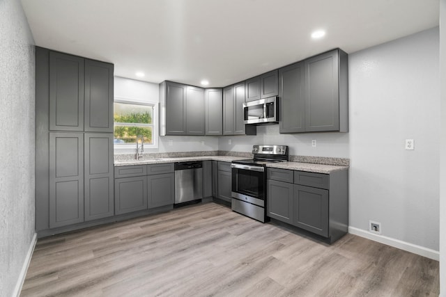 kitchen featuring baseboards, light wood-type flooring, appliances with stainless steel finishes, and gray cabinetry