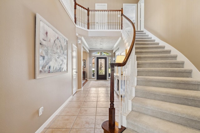 entrance foyer featuring tile patterned floors, ornamental molding, stairway, baseboards, and a towering ceiling