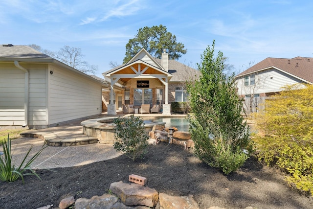 rear view of property with an outdoor pool, a jacuzzi, a patio, and a chimney