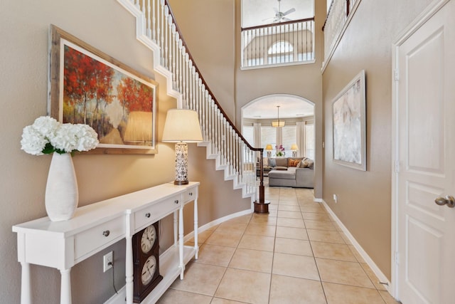 foyer with baseboards, ceiling fan, stairway, light tile patterned floors, and arched walkways