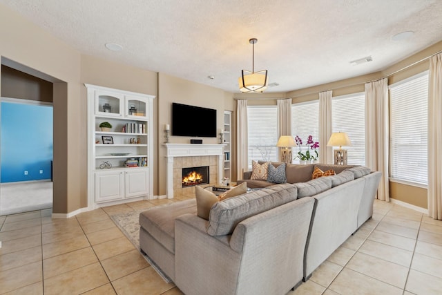 living room with visible vents, a tiled fireplace, a textured ceiling, light tile patterned floors, and baseboards