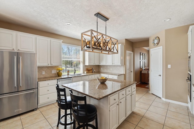 kitchen with stainless steel appliances, a kitchen island, light tile patterned flooring, and white cabinetry