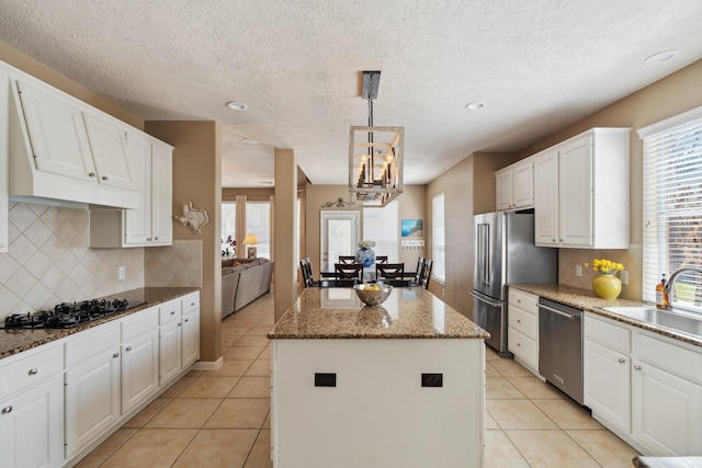 kitchen with a kitchen island, light tile patterned flooring, a sink, stainless steel appliances, and white cabinets