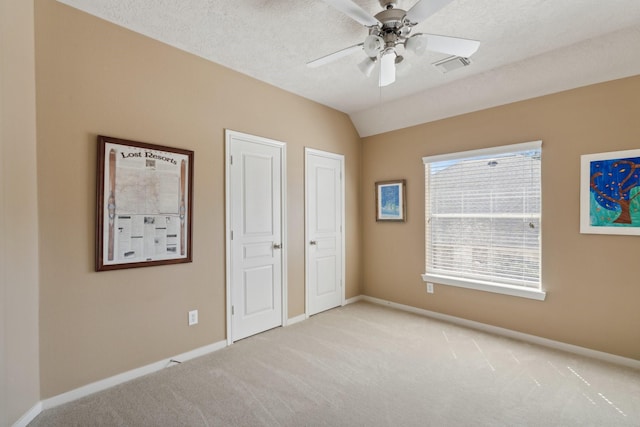 unfurnished bedroom with light carpet, visible vents, baseboards, and vaulted ceiling