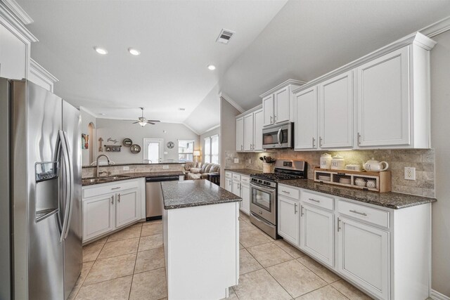 kitchen with lofted ceiling, a sink, stainless steel appliances, tasteful backsplash, and a center island