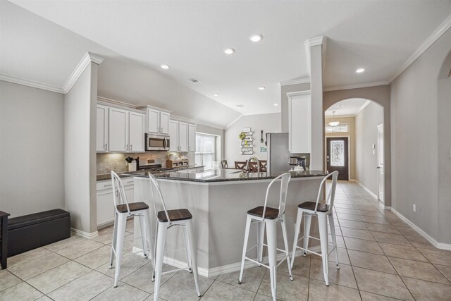 kitchen featuring arched walkways, stainless steel appliances, white cabinetry, a kitchen breakfast bar, and tasteful backsplash