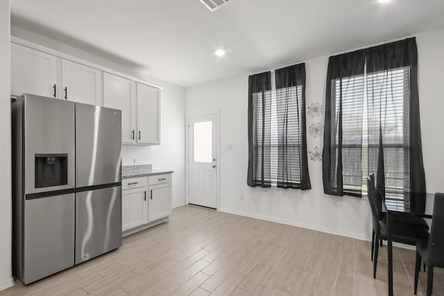 kitchen featuring white cabinetry, stainless steel fridge, light wood finished floors, baseboards, and light stone countertops