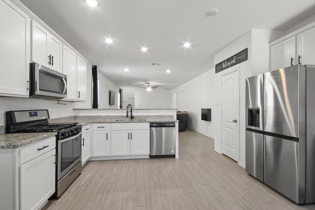 kitchen with a sink, a peninsula, white cabinets, and stainless steel appliances