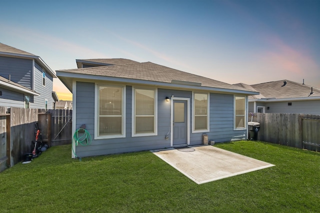 back of house at dusk with a patio area, a yard, a fenced backyard, and roof with shingles