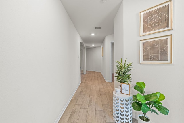 corridor with light wood-type flooring, visible vents, recessed lighting, arched walkways, and baseboards