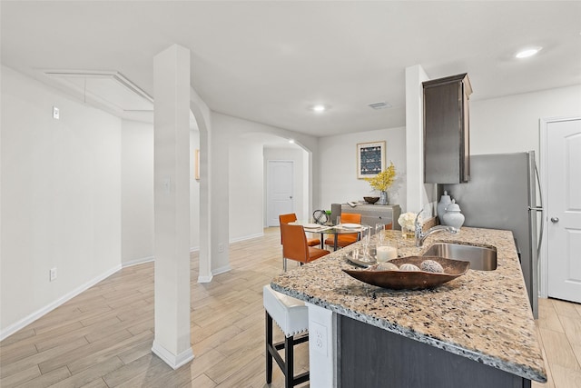 kitchen featuring arched walkways, light wood-style flooring, a kitchen bar, and light stone counters