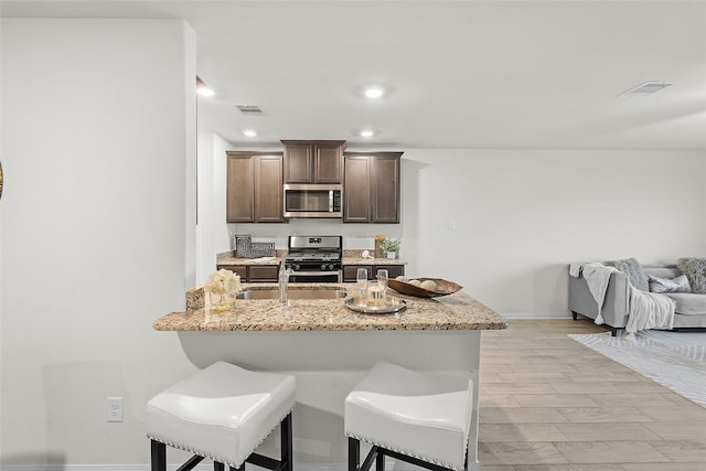 kitchen featuring visible vents, dark brown cabinetry, appliances with stainless steel finishes, and a breakfast bar area