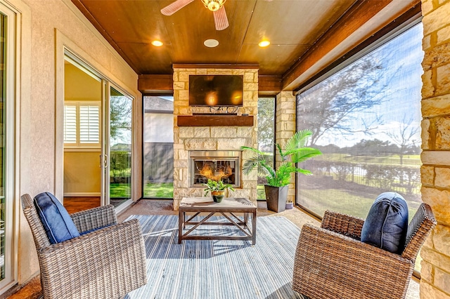 sunroom with an outdoor stone fireplace and ceiling fan