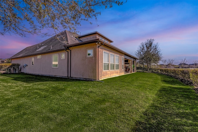 back of property at dusk featuring a yard and stucco siding