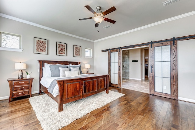 bedroom featuring visible vents, ornamental molding, a barn door, and hardwood / wood-style flooring