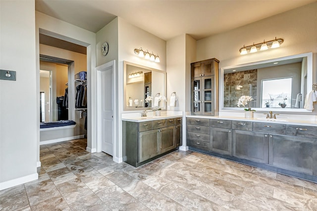 full bath with baseboards, tiled shower, two vanities, a sink, and a walk in closet