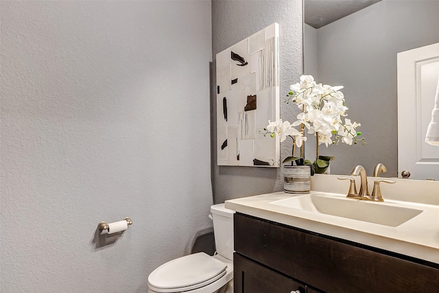 bathroom with toilet, vanity, and a textured wall