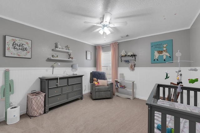 carpeted bedroom featuring visible vents, a textured ceiling, and a wainscoted wall