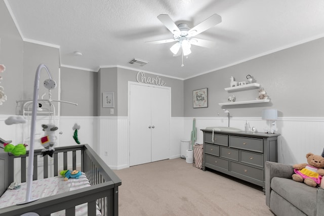 bedroom featuring a textured ceiling, light carpet, visible vents, and wainscoting