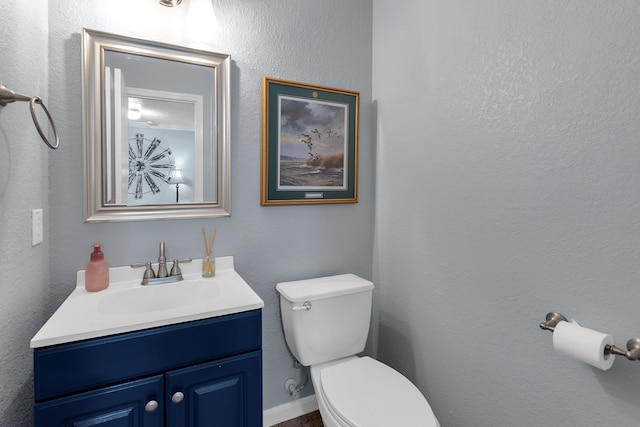 bathroom featuring toilet, vanity, and a textured wall