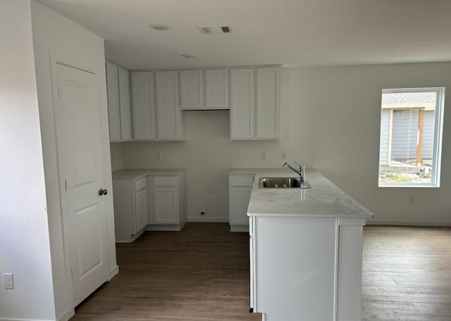 kitchen with visible vents, baseboards, a peninsula, light wood-style floors, and a sink