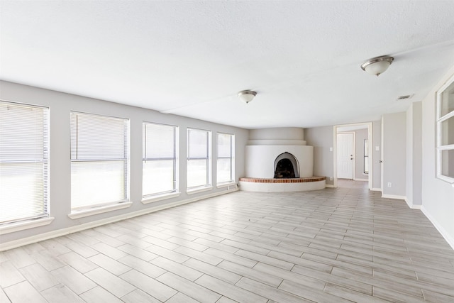 unfurnished living room with visible vents, a fireplace with raised hearth, a textured ceiling, and baseboards