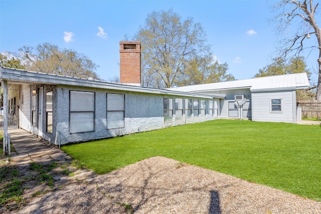 back of house featuring a chimney, a yard, and metal roof