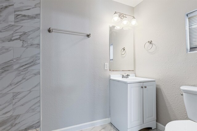 bathroom with vanity, toilet, a textured wall, and baseboards