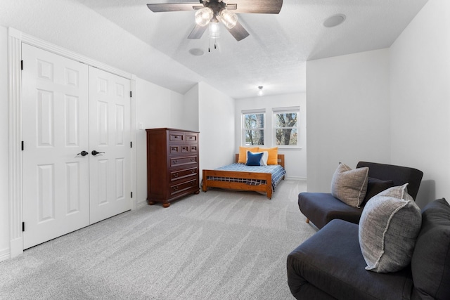 bedroom with a closet, light colored carpet, ceiling fan, and a textured ceiling