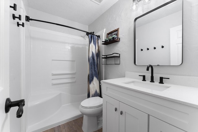 bathroom with toilet, a textured ceiling, wood finished floors, vanity, and a textured wall