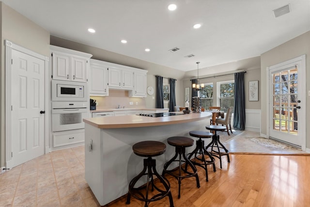 kitchen with white appliances, a kitchen island, an inviting chandelier, light countertops, and white cabinets