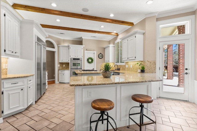 kitchen featuring a breakfast bar area, light stone counters, appliances with stainless steel finishes, a peninsula, and white cabinets