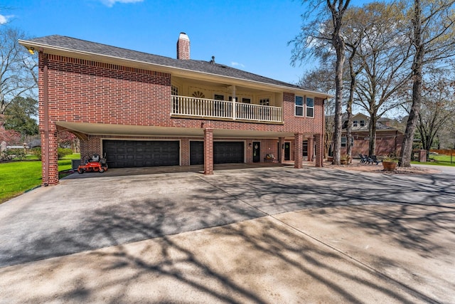 rear view of house with brick siding, concrete driveway, a chimney, a balcony, and an attached garage