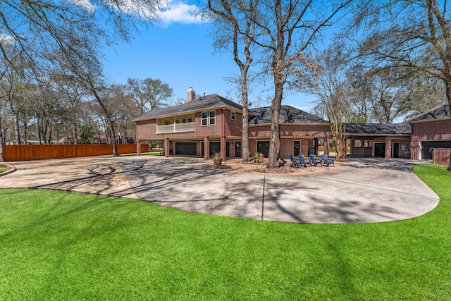 back of property with a yard, concrete driveway, an attached garage, brick siding, and a chimney