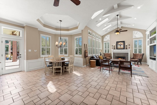 dining space with a glass covered fireplace, crown molding, ceiling fan with notable chandelier, and wainscoting