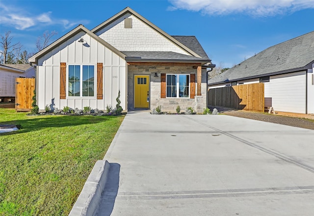 view of front of property with concrete driveway, fence, board and batten siding, and a front yard