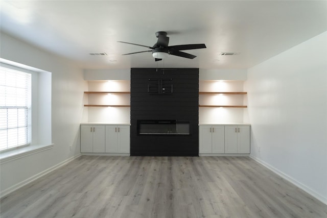 unfurnished living room with visible vents, light wood-style flooring, a large fireplace, and ceiling fan