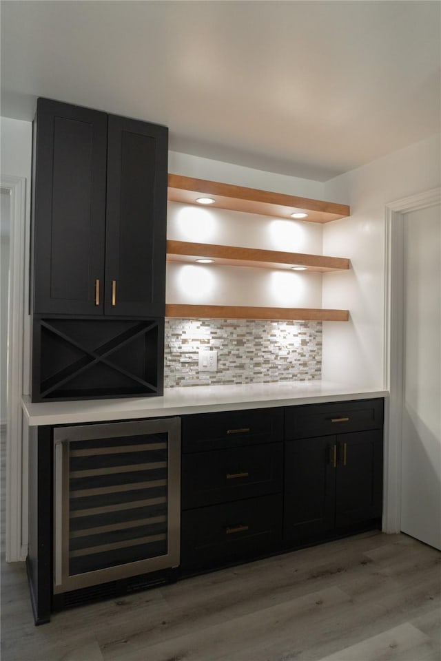 bar featuring beverage cooler, light wood-style floors, and backsplash