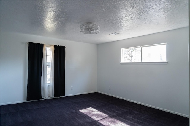 spare room featuring visible vents, a healthy amount of sunlight, baseboards, and dark colored carpet