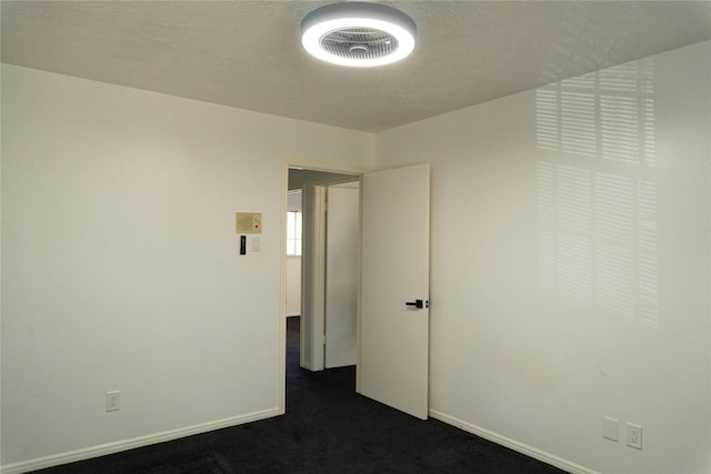 spare room featuring dark colored carpet and baseboards